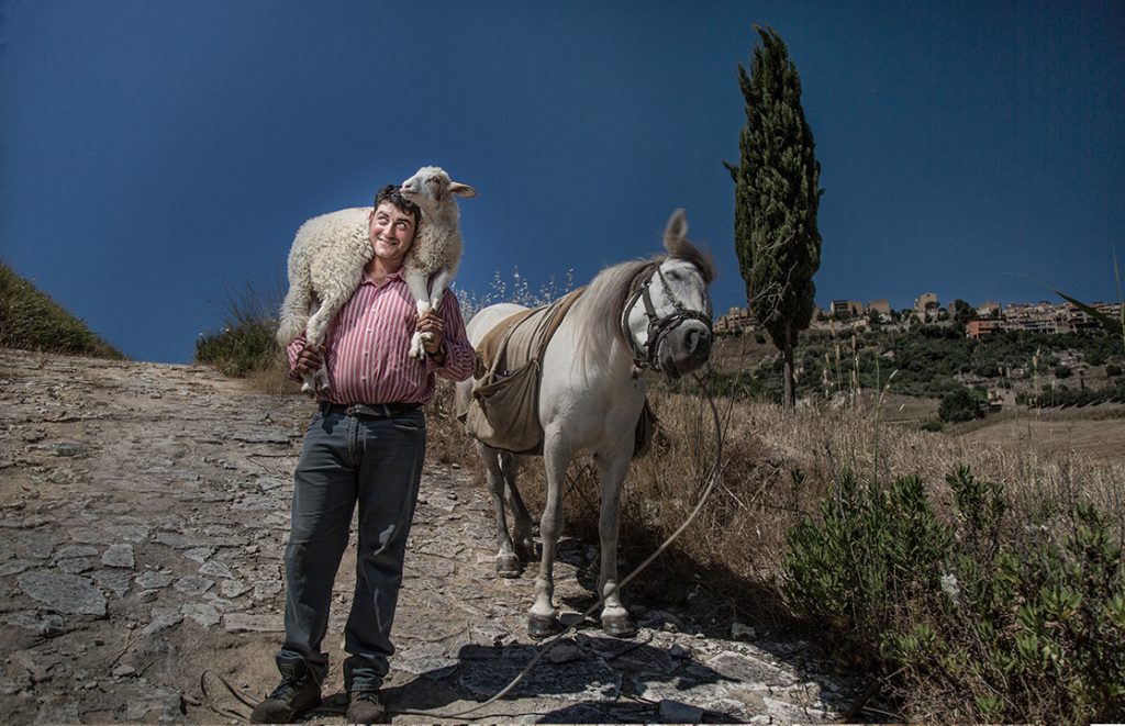 man with sheep on shoulders standing in front of donkey